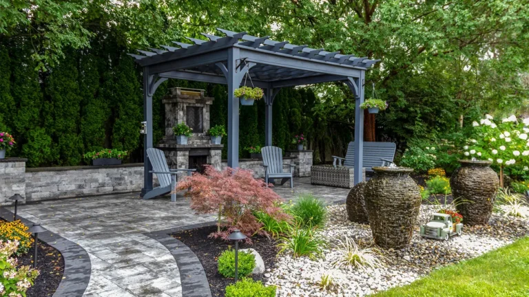 Outdoor living area ideas should include wooden pergolas and pavers, such as what's pictured here in a yard with a mixture of grass, gravel, and vegetation.